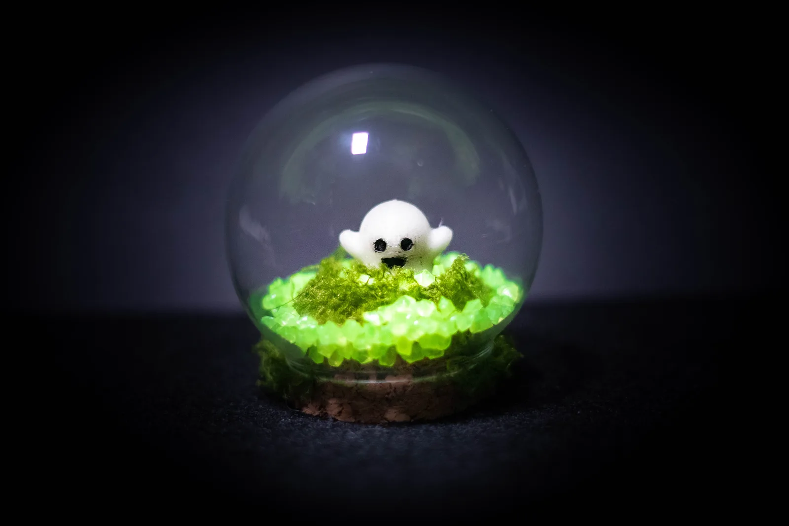 Glass dome terrarium with a small white ghost on moss and glowing green stones