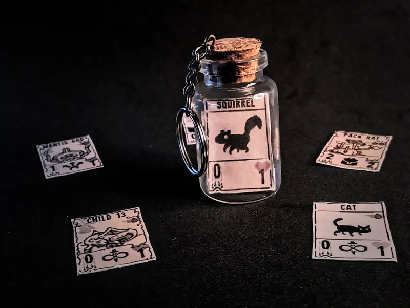 Corked glass bottle keychain holding a miniature Inscryption Squirrel card, with more mini cards around it