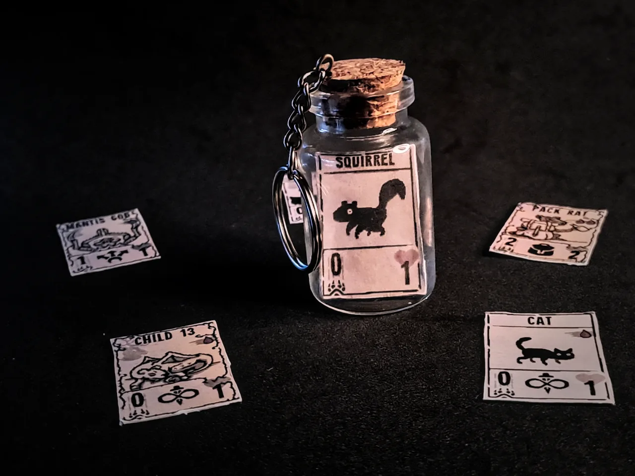 Corked glass bottle keychain holding a miniature Inscryption Squirrel card, with more mini cards around it