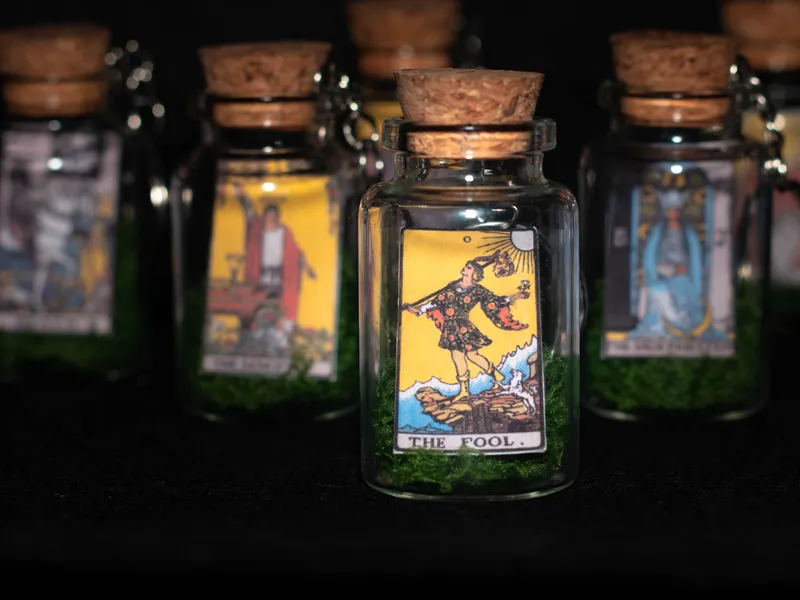 Corked glass bottle keychains, each holding a miniature tarot card on green moss