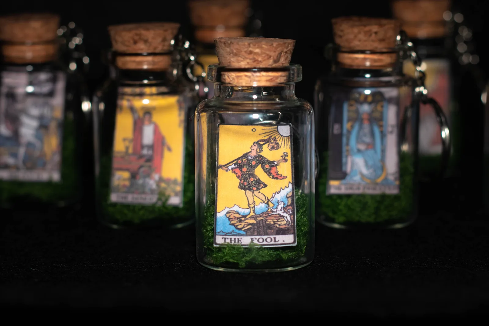 Corked glass bottle keychains, each holding a miniature tarot card on green moss